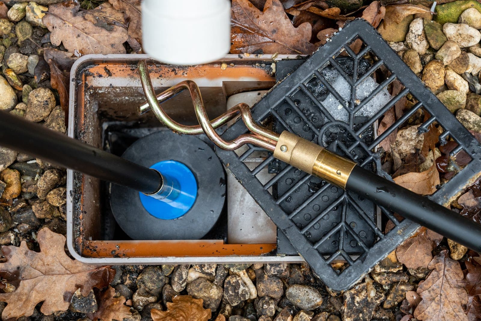 An engineer clearing a blocked outdoor drainage gully with drain rods outside a Yorkshire home